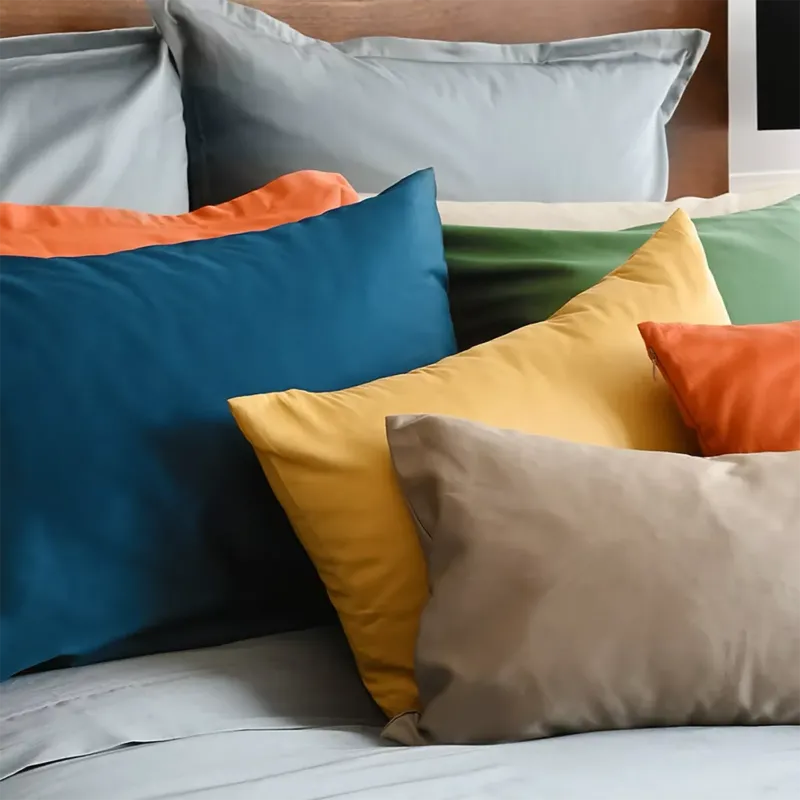 Capri Sateen pillowcases in teal, gold, orange, green, and taupe styled on a bed.