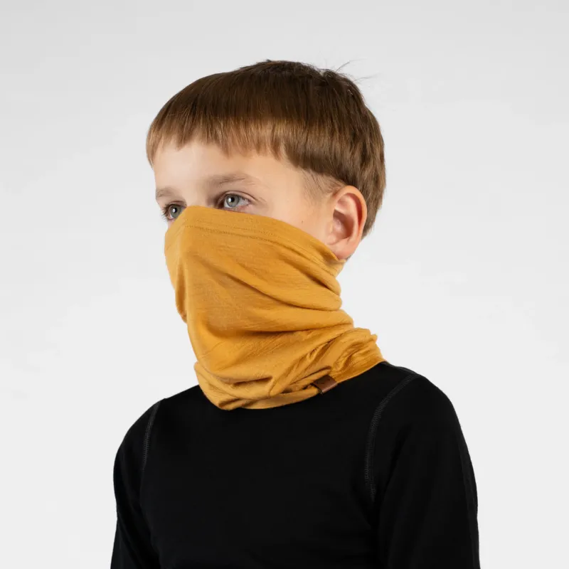A close-up portrait of a young boy looking off to his left in a three-quarter profile against a white background. He is wearing a black long-sleeved top and a mustard yellow neck gaiter pulled up over his nose and mouth, showing how it bunches comfortably around his neck.