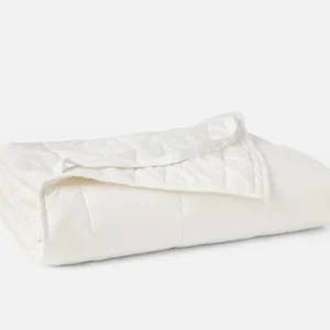 Coyuchi Washable Wool Filled Mattress Topper in white, neatly folded showing quilted texture.