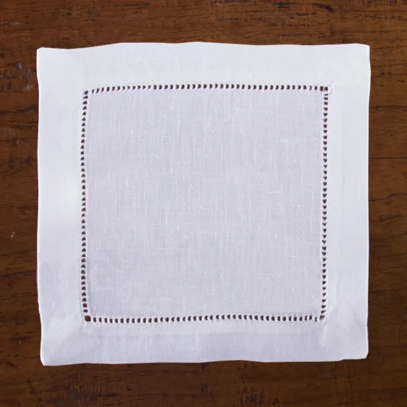 A set of four white Henry Handwork Heirloom Estate cocktail napkins with hemstitch borders, shown flat on a wooden surface.