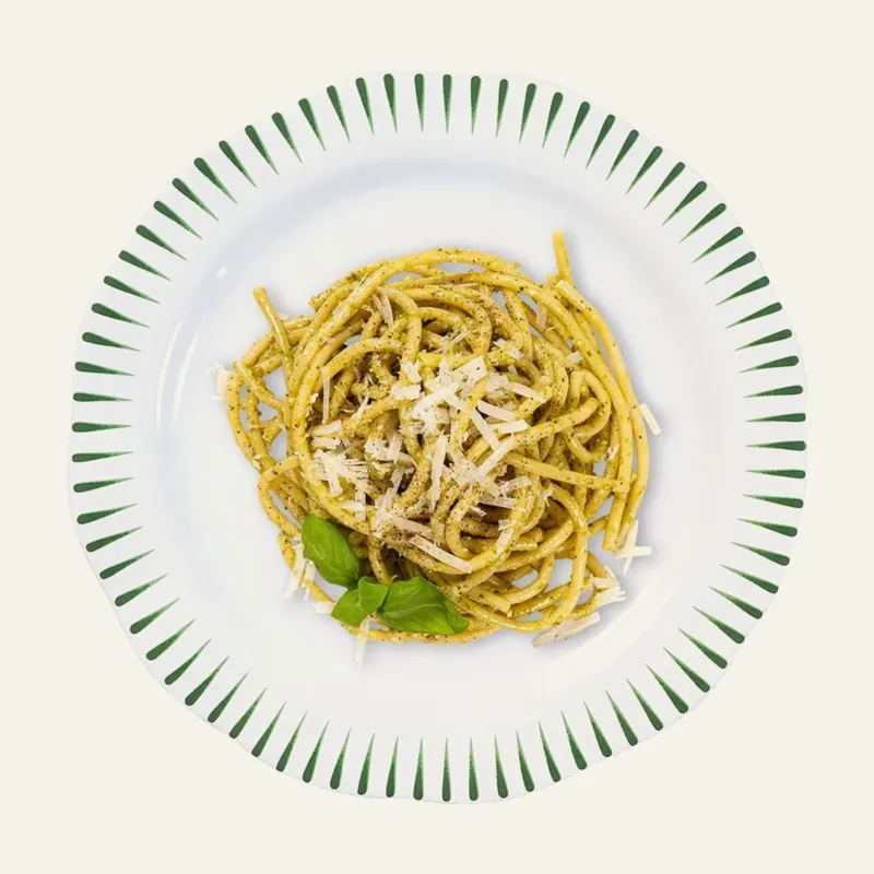 Juliska Sitio Stripe dinner plate with pesto pasta and shaved parmesan, green stripe rim.