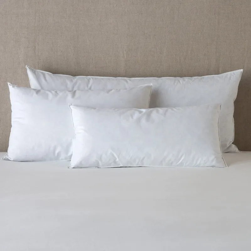 Multiple white Bella Notte Essential Down pillow inserts styled on a neutral linen bed, various sizes.