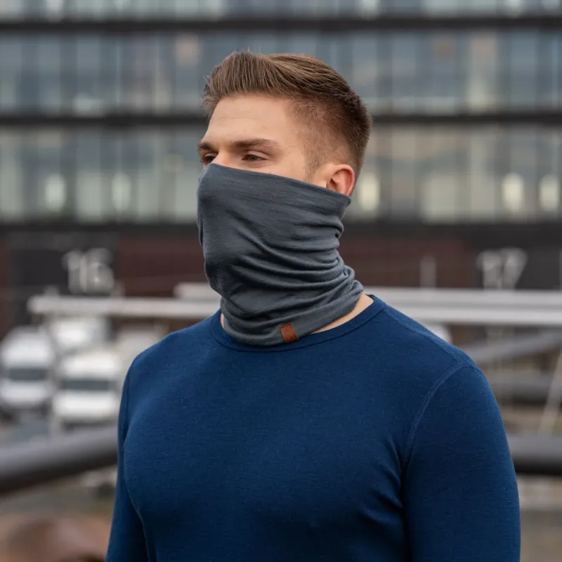 A man wearing the menique unisex neck gaiter in perfect gray color. He is outside, dressed in a long sleeve merino top in dark blue color.