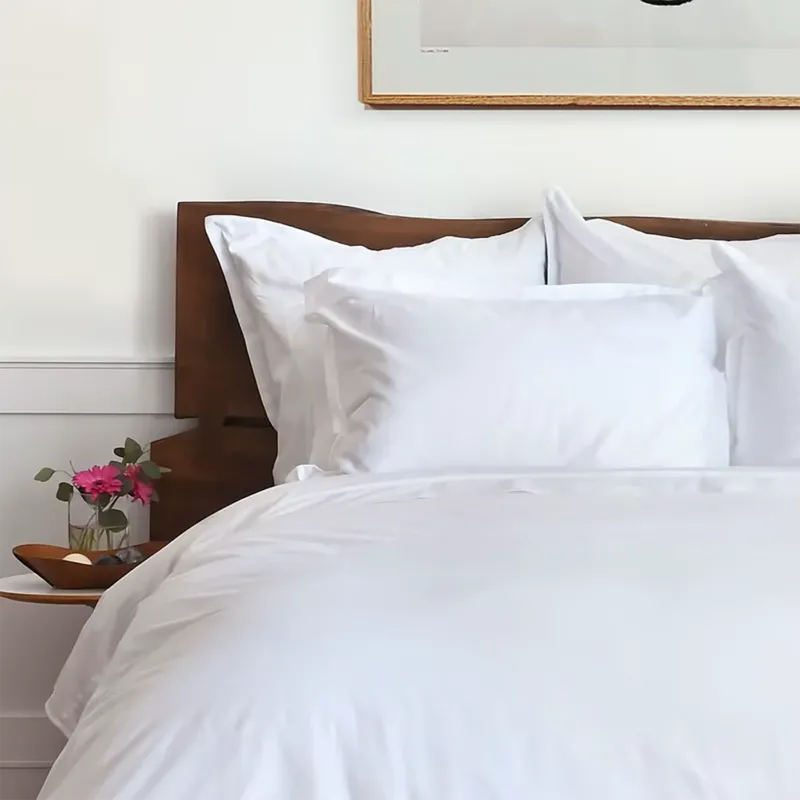 St. Geneve Capri Sateen fitted sheet in white, styled on a bed with wood headboard.