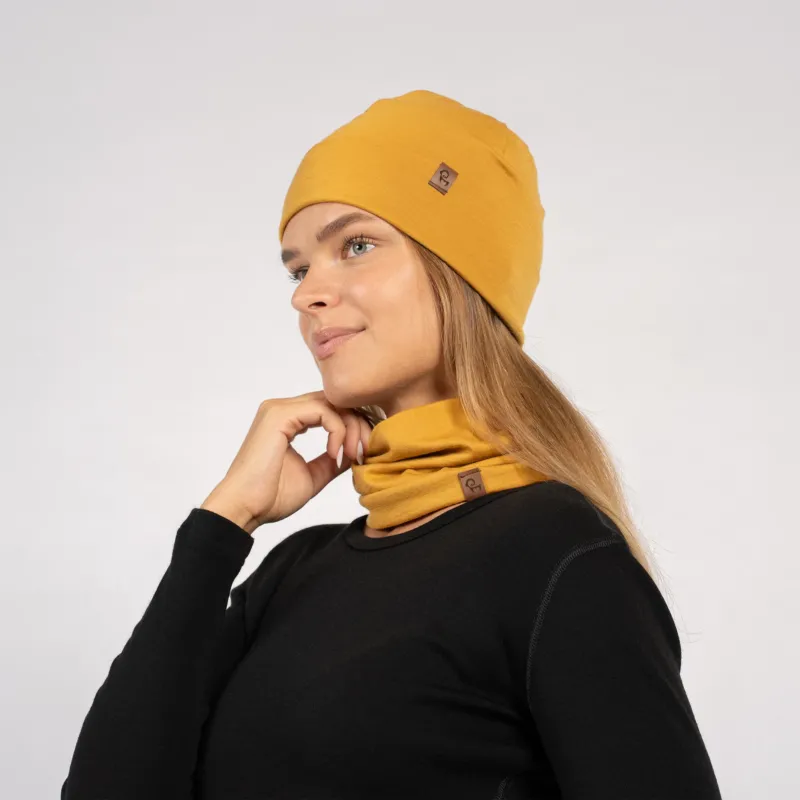 Woman in yellow Merino beanie and gaiter worn around neck, posing in black long sleeve top – side view.