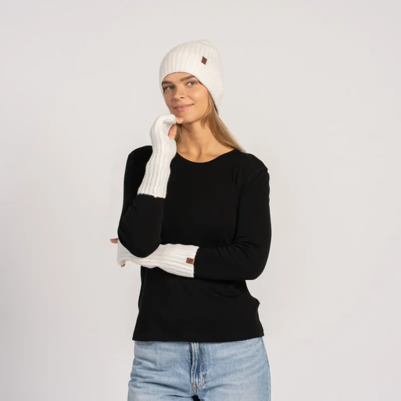 Full-length shot of woman in black top and jeans wearing white beanie and long white wrist warmers, facing camera.