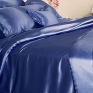 A bed dressed in Kumi Kookoon's Classic Silk King Duvet Cover, featuring smooth, shiny blue charmeuse silk bedding and pillowcases with a soft fold.
