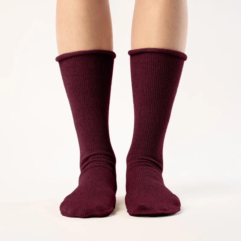 A person is shown from the mid-thigh down, wearing ribbed, royal cherry colos socks. The socks are pulled up to the mid-calf, and the person's feet are slightly apart against a plain white background. The lighting is even, highlighting the texture of the socks.