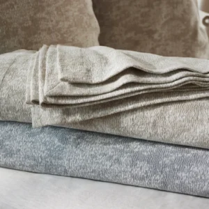 SDH Bellini decorative pillows stacked with folded blankets in taupe and slate blue.